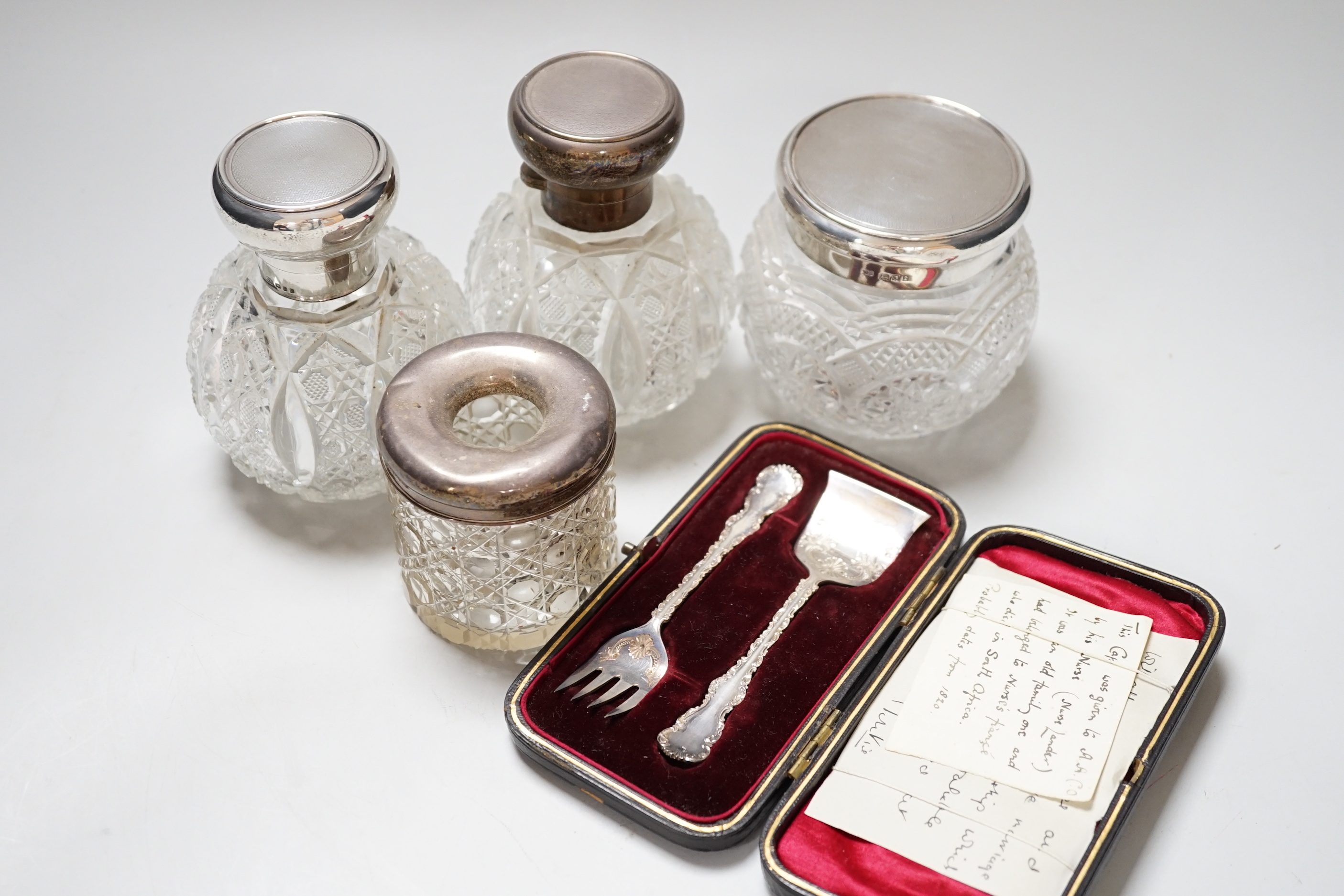A pair of George V silver mounted cut glass scent bottles, London 1920, 11cm, a similar toilet jar, a hair tidy and a cased two piece christening set
